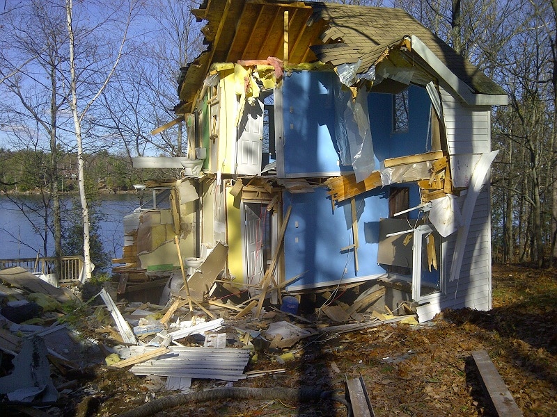 A half-demolished cottage sits near a lakefront in the autumn.
