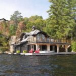 A luxury black boathouse features a peaked roof and a spacious second-story deck above the dock and boat slips.