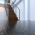 Floodwater covering the floor of a modern home interior at the base of a wooden staircase, needing flood repair.