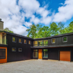 Modern black custom home in Cottage Country with wood garage doors and forest views.
