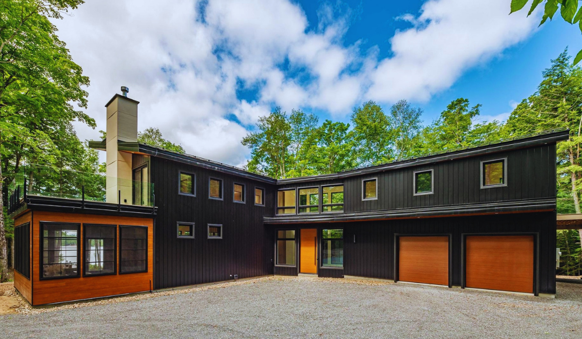 Modern black custom home in Cottage Country with wood garage doors and forest views.