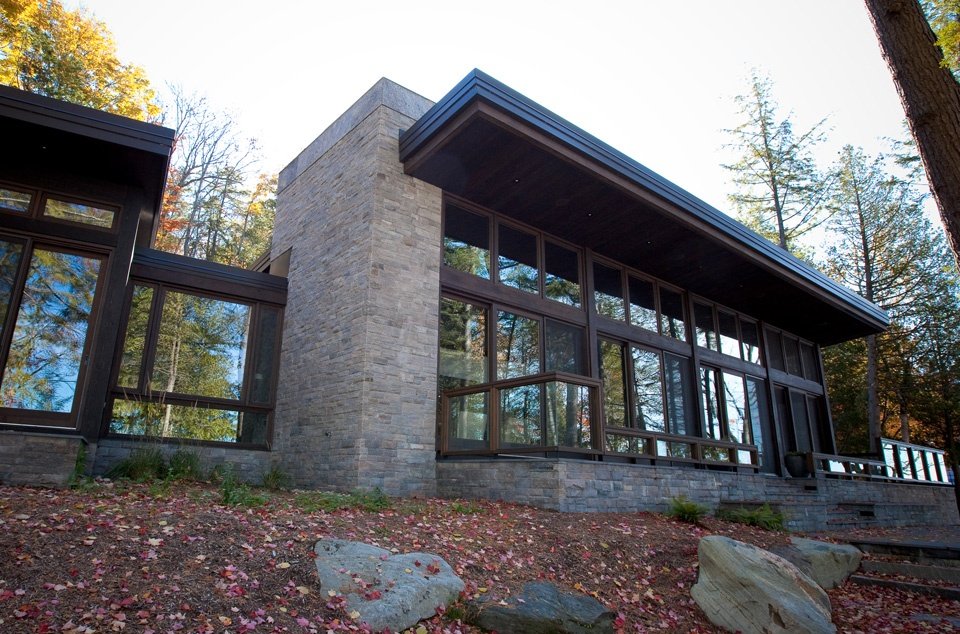 large glass framing on the back side of a cottage surrounded by trees