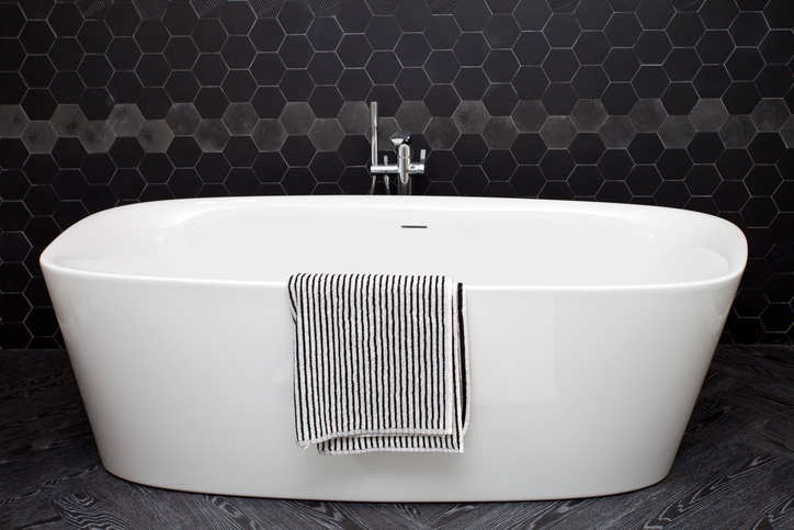 Bathtub sitting next to wall of black honeycomb tiles, with a zigzagging row of light tiles running along center of the wall.