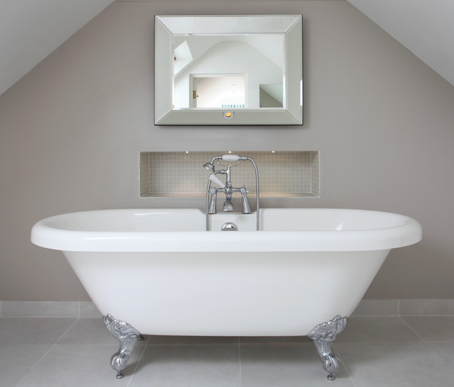 A freestanding bathtub with ornate feet sits beneath a square mirror.