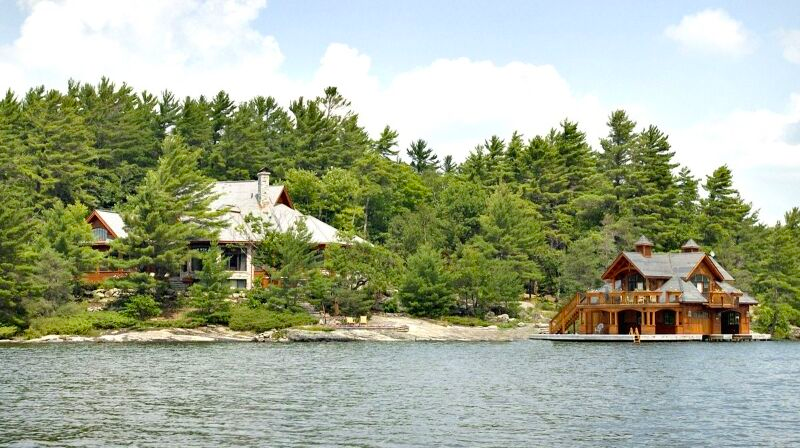 A large luxury home and boathouse sit on a lakeshore in Ontario cottage country. The scene is beautiful, but oh so expensive.