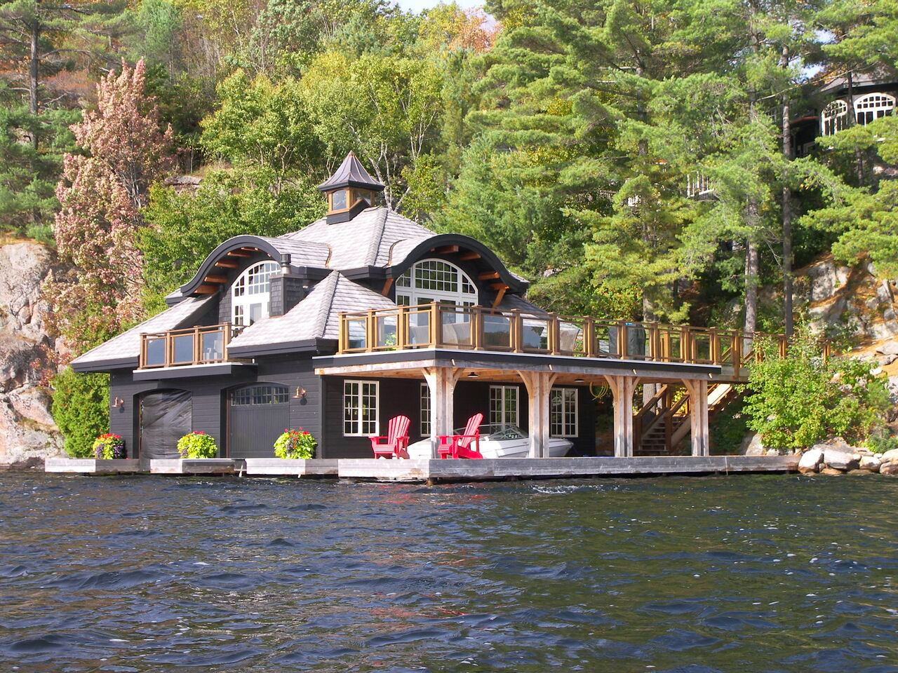 A boathouse sits on a lake in Ontario cottage country, down from a luxury home, just barely visible in a corner of the image.
