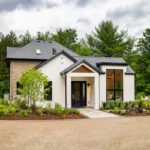 A modern white cottage with black trim and landscaped gardens set against a forest backdrop in Muskoka.